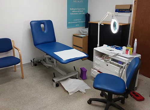 Diane's treatment room at Wallingford Sports Park, with a blue treatment couch, chairs and a magnifying lamp
